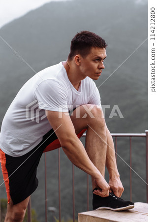 Handsome muscular hunk man looking at mountains from the peak. 114212800
