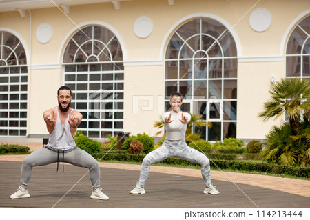 Sporty couple are worming up against urban building in park Sporty couple are worming up against urban building in park 114213444