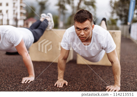 Two young athletes doing push-ups outdoors. 114213551