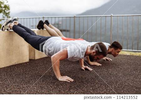 Two young athletes doing push-ups outdoors. 114213552