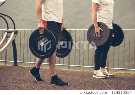 Caucasian muscular men with weight plates preparing to outdoor workout. 114213594