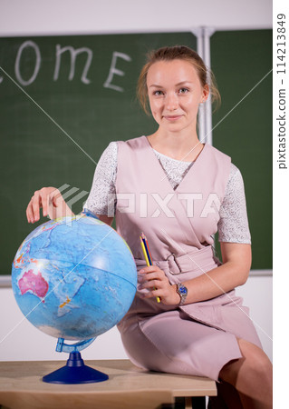 young teacher looking away at desk with globe young teacher looking away at desk with globe 114213849