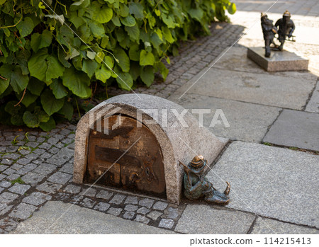 Small copper statue of a goblin, sitting on the floor of a street in Wroclaw, Poland. Hunting for dwarfs, tourist attraction. 114215413
