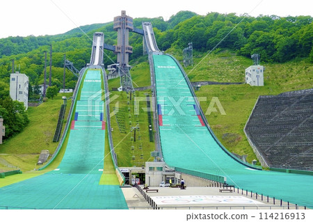 A view of the normal hill and large hill at Hakuba Ski Jumping Stadium, with a vivid green sky and no snow. Hakuba Village, Nagano Prefecture. A view of the normal hill and large hill at Hakuba Ski Jumping Stadium, with a vivid green sky and no snow. Hakuba Village, Nagano Prefecture. 114216913