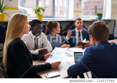 Multiracial business team in office analyze data on charts, diagrams. Caucasian woman, African man, and colleagues plan strategies. Corporate group discuss growth, sales, marketing ideas in meeting. Multiracial business team in office analyze data on charts, diagrams. Caucasian woman, African man, and colleagues plan strategies. Corporate group discuss growth, sales, marketing ideas in meeting. 114217749