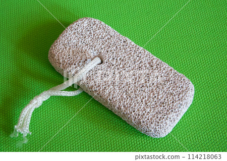 Skincare Tool Display. Pumice stone with string, presented on vibrant green, highlighting its exfoliating texture. Skincare Tool Display. Pumice stone with string, presented on vibrant green, highlighting its exfoliating texture. 114218063
