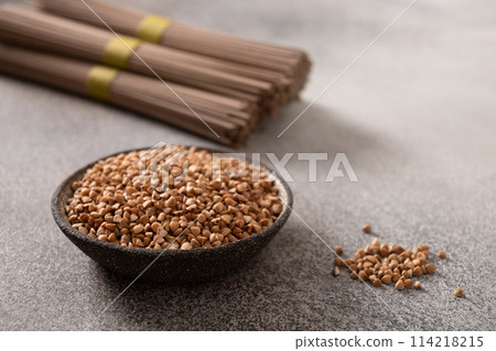 Uncooked buckwheat noodles soba and grain ion bowl on gray background. Space for text. Healthy vegan diet. Close up. Alternative gluten free pasta. Uncooked buckwheat noodles soba and grain ion bowl on gray background. Space for text. Healthy vegan diet. Close up. Alternative gluten free pasta. 114218215
