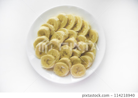 Sliced bananas on a white plate. Delicious and juicy fruits. Breakfast on a plate. 114218940
