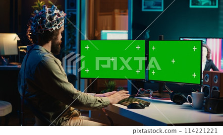 Computer engineer using EEG headset, starting mind upload process using green screen PC. Man using neuroscientific device to transfer consciousness into cyberspace with mockup monitors, camera A 114221221