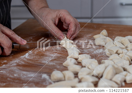 Female hands knead the dough and cut it on a wooden table.Female hands knead  114221587