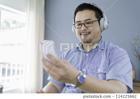 一個大個子的日本男人一邊聽音樂一邊看他的智慧型手機 一個大個子的日本男人一邊聽音樂一邊看他的智慧型手機 114225662