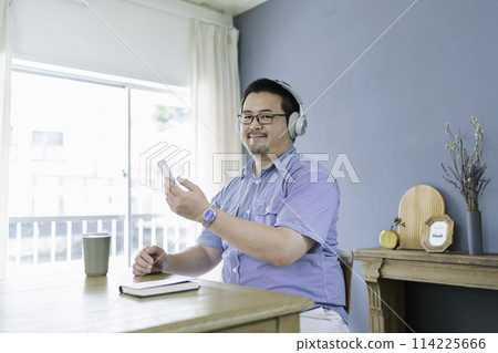 A large Japanese man listening to music while looking at his smartphone A large Japanese man listening to music while looking at his smartphone 114225666