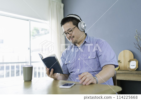 A large Japanese man reading a book and listening to music A large Japanese man reading a book and listening to music 114225668
