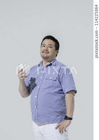 A large Japanese man listening to music on his smartphone 114225864