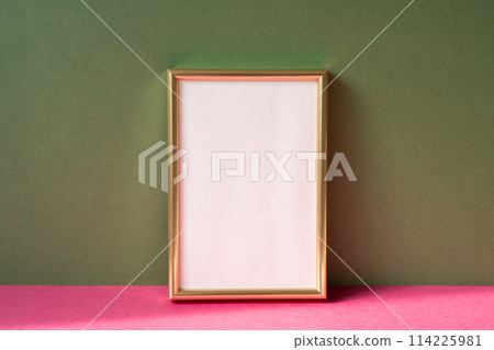 Gold picture frame with copy space on pink table. khaki green wall background Gold picture frame with copy space on pink table. khaki green wall background 114225981