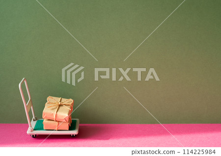 Trolley cart with gift boxes on pink and khaki green background. Parcel Delivery Concept 114225984