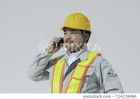 A man in work clothes making a phone call on his smartphone A man in work clothes making a phone call on his smartphone 114226066
