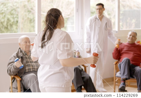 Physiotherapist explaining the exercises to a group of seniors 114229269