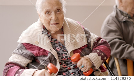 Old woman exercising with dumbbells sitting on a nursing home 114229270