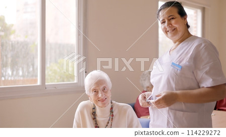 Caregiver smiling at camera next to old people in geriatric 114229272