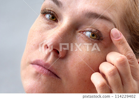 Middle aged caucasian woman of 40s holding fingers on eyelids to show eyes aging Middle aged caucasian woman of 40s holding fingers on eyelids to show eyes aging 114229402