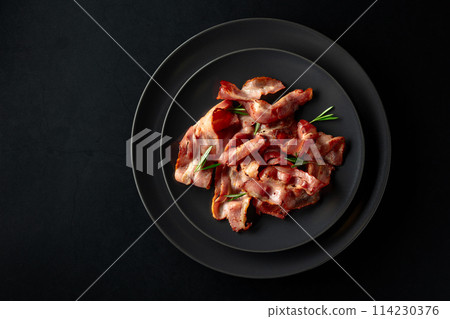 Roasted bacon slices with rosemary on a black plate. 114230376