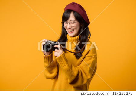 A stylish photographer, a young Asian woman in a yellow sweater and red beret, takes artistic shots with her camera, crafting memories against a cheerful yellow background. A stylish photographer, a young Asian woman in a yellow sweater and red beret, takes artistic shots with her camera, crafting memories against a cheerful yellow background. 114233273