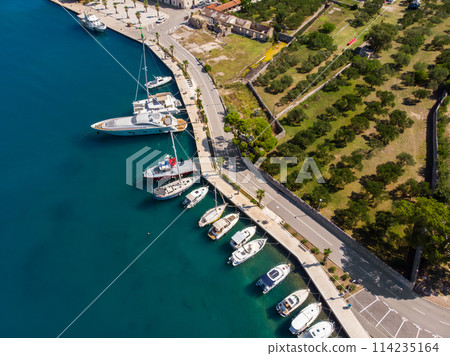 Scenic aerial view many yachts boats moored at Croatian bay harbor shore blue turquoise clear water at bright summer sunny day. Top above Mediterranean sea marina. Boat vessel charter service Scenic aerial view many yachts boats moored at Croatian bay harbor shore blue turquoise clear water at bright summer sunny day. Top above Mediterranean sea marina. Boat vessel charter service 114235164