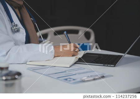 Female doctor sitting at desk and writing a prescription for her patient Female doctor sitting at desk and writing a prescription for her patient 114237256