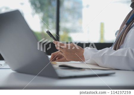 Female doctor sitting at desk and writing a prescription for her patient 114237259