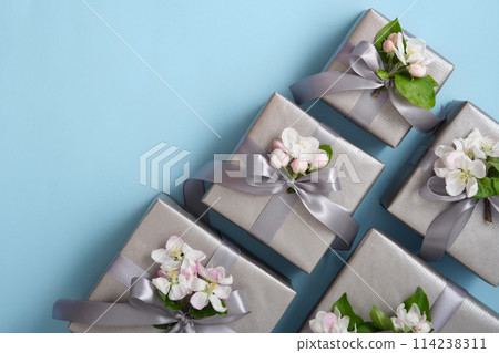 Gray gift boxes with apple flowers and silver ribbons on light blue background. Horizontal, space for your text. 114238311