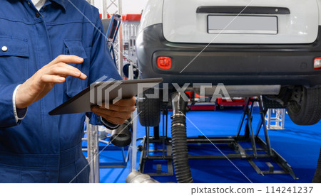 Serviceman with digital tablet on the background of the car in the car service. Serviceman with digital tablet on the background of the car in the car service. 114241237