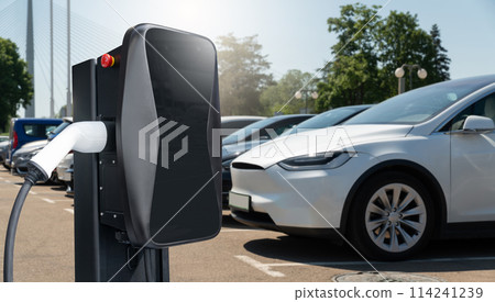 Electric vehicles charging station on a background of a row of cars. Concept Electric vehicles charging station on a background of a row of cars. Concept 114241239