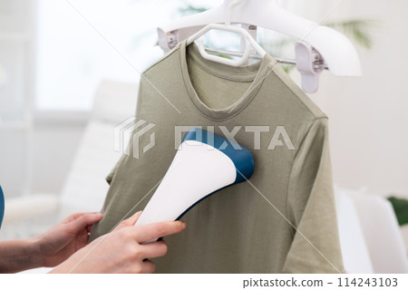 Cropped woman using steaming iron to ironing fashion shirt at home in bright cozy room. Female holding electric steamer Cropped woman using steaming iron to ironing fashion shirt at home in bright cozy room. Female holding electric steamer 114243103