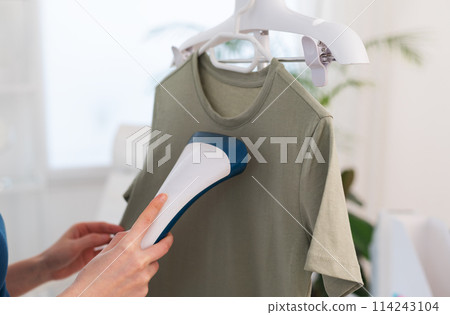 Using steaming iron to ironing t-shirt in home. Doing stream vapor iron for press clothes in hand. Using steaming iron to ironing t-shirt in home. Doing stream vapor iron for press clothes in hand. 114243104