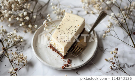 poppy seed cheesecake on plate with a fork against a white background with dried flowers 114243126