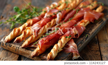 Bunch of traditional italian Grissini breadsticks wrapped parma ham, prosciutto with fresh herbs on a wooden board, close up view 114243127