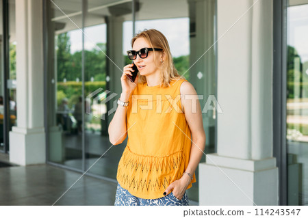 Happy blonde 30s woman in sunglasses talking phone and look happy outdoors Urban lifestyle concept. Summer time Happy blonde 30s woman in sunglasses talking phone and look happy outdoors Urban lifestyle concept. Summer time 114243547