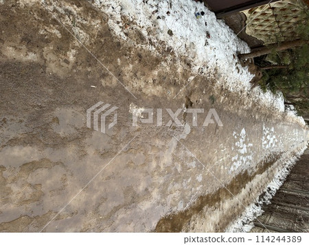 Melting dirty snow on the streets of the city during the daytime in winter. The pedestrian road is snow with sand and mud. Traces of people and pets. Melting dirty snow on the streets of the city during the daytime in winter. The pedestrian road is snow with sand and mud. Traces of people and pets. 114244389