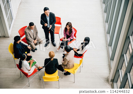 Top view of multiethnic professionals in bustling office engaged in teamwork and discussions. Businessman and businesswoman sit at conference leaving copy space. dynamic business meeting in progress. 114244832