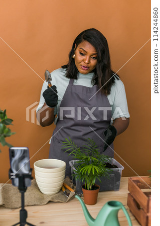 African american florist blogger filming tutorial video about transplanting plants in home garden. Make video vlog with mobile phone 114244860
