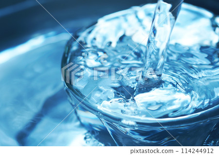 Water falling vigorously into a glass 114244912