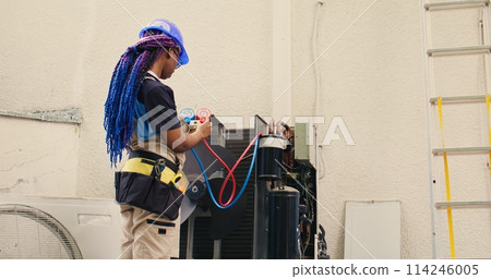 Skilled african american expert looking at freon levels in air conditioner while using manifold indicators to measure the pressure in HVAC system, ensuring efficient cooling performance 114246005