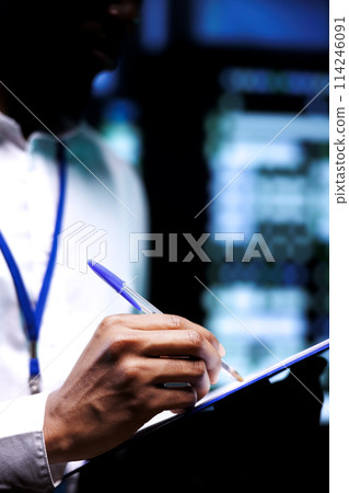 Serviceman conducts comprehensive diagnostic assessments on server hub to uncover and rectify underlying issues with data center equipment. Manager attentively reviewing maintenance checklist 114246091