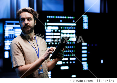 Repairman doing routine system servicing, imputing data on tablet of required upkeeping in server rigs housing advanced data storage infrastructure supporting critical IT workloads 114246125