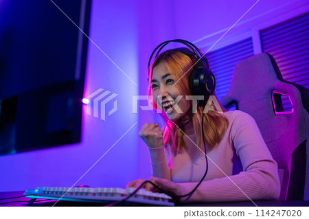 Winning. Happy Gamer young plays online video games computer she raises hands to wins tournament, young woman in gaming headphones playing video game online at home feel excited, E-Sport concept Winning. Happy Gamer young plays online video games computer she raises hands to wins tournament, young woman in gaming headphones playing video game online at home feel excited, E-Sport concept 114247020