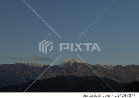 The moon above the ridge of Mount Kaikoma in the Southern Alps as the morning sun shines 114247874
