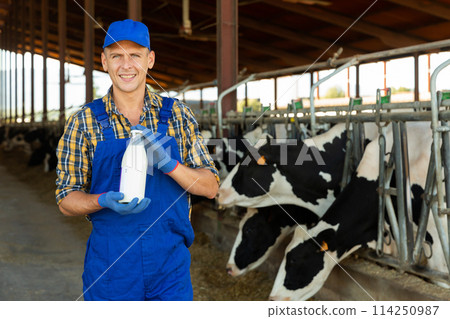Successful farmer standing in cowshed at dairy farm with bottle of milk Successful farmer standing in cowshed at dairy farm with bottle of milk 114250987