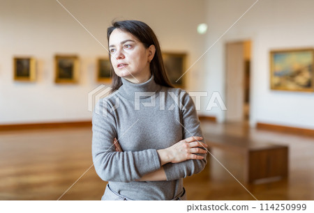 Interested woman visiting exhibition of paintings in art museum Interested woman visiting exhibition of paintings in art museum 114250999
