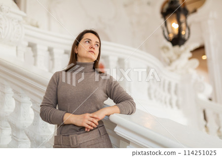 Interested woman standing near stucco railings on stairs in antique palace 114251025